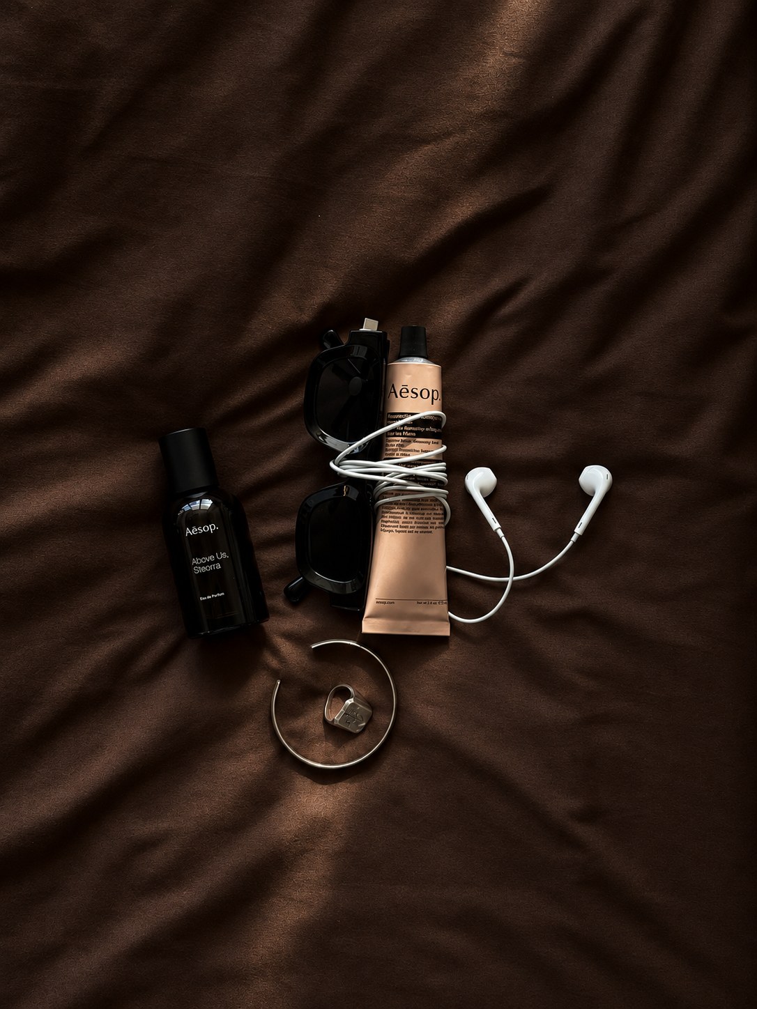 Editorial still life with Aesop products, sunglasses, earphones, and jewelry