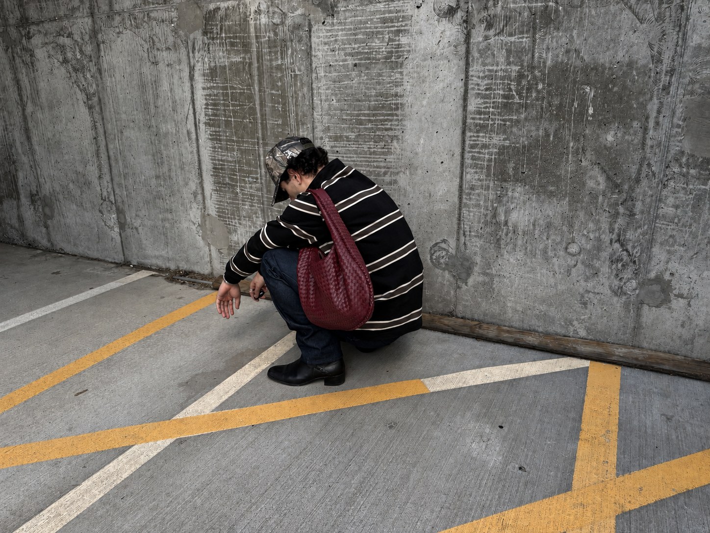 Luis Corrales in a striped look with a burgundy woven bag against a concrete wall